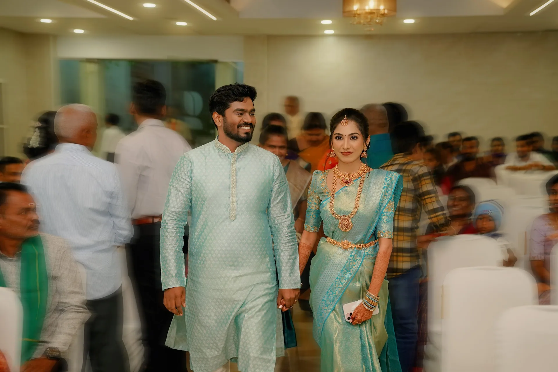 Saran and Monisha holding hands among guests at their engagement in Chennai.