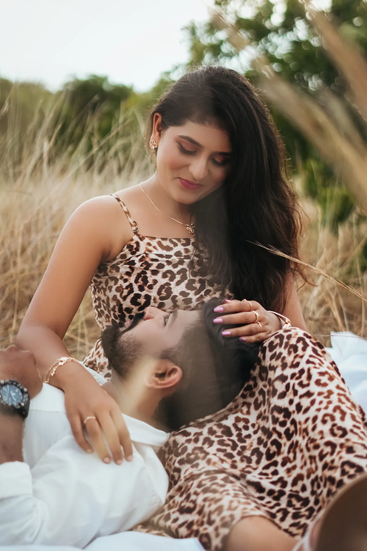 Pre-wedding couple on a picnic sheet beside a camera in the ECR dune grass, Chennai — LNC Photography.