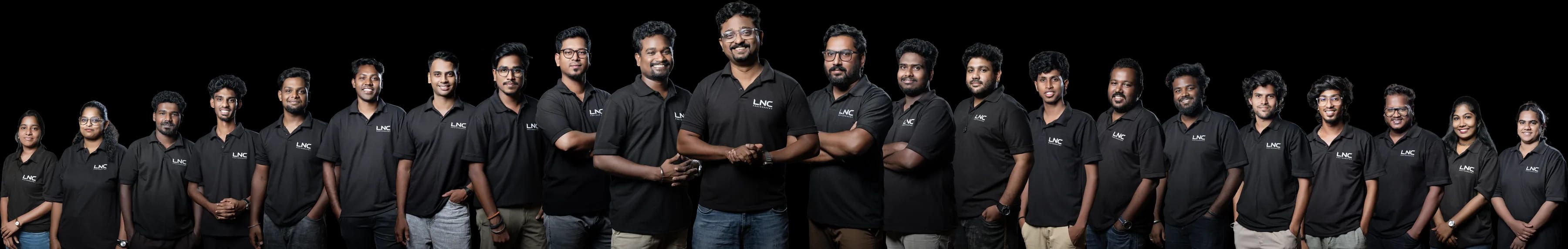The LNC Photography team — photographers, cinematographers and editors in black LNC polo shirts, standing in a wide arc against a dark studio backdrop, Chennai.